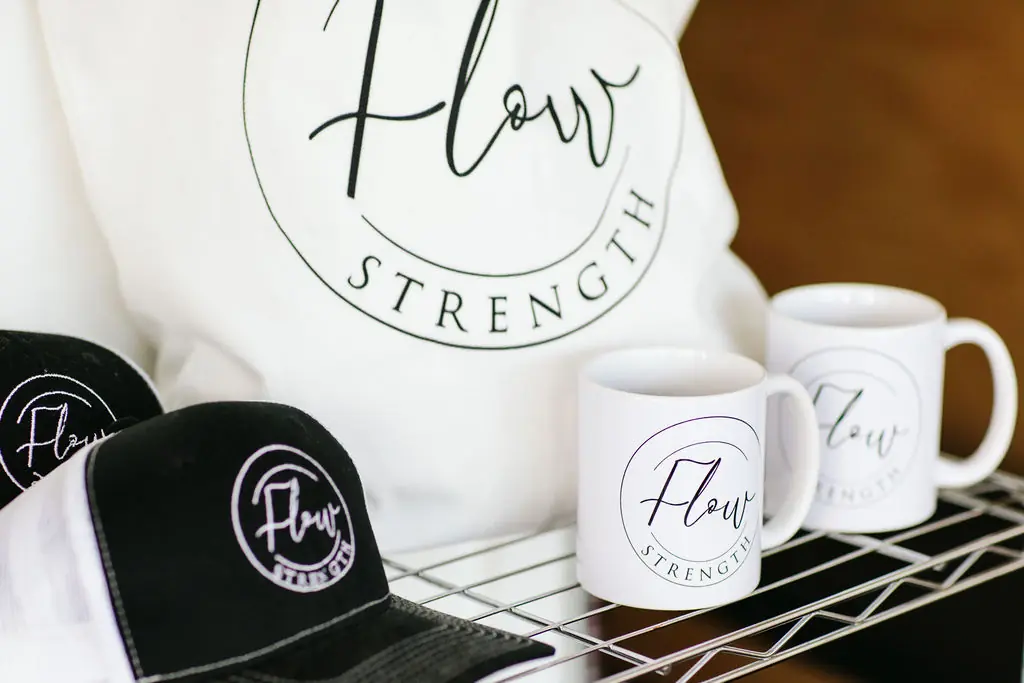 Flow Strength tote bag, caps and mugs arranged on the merch shelf