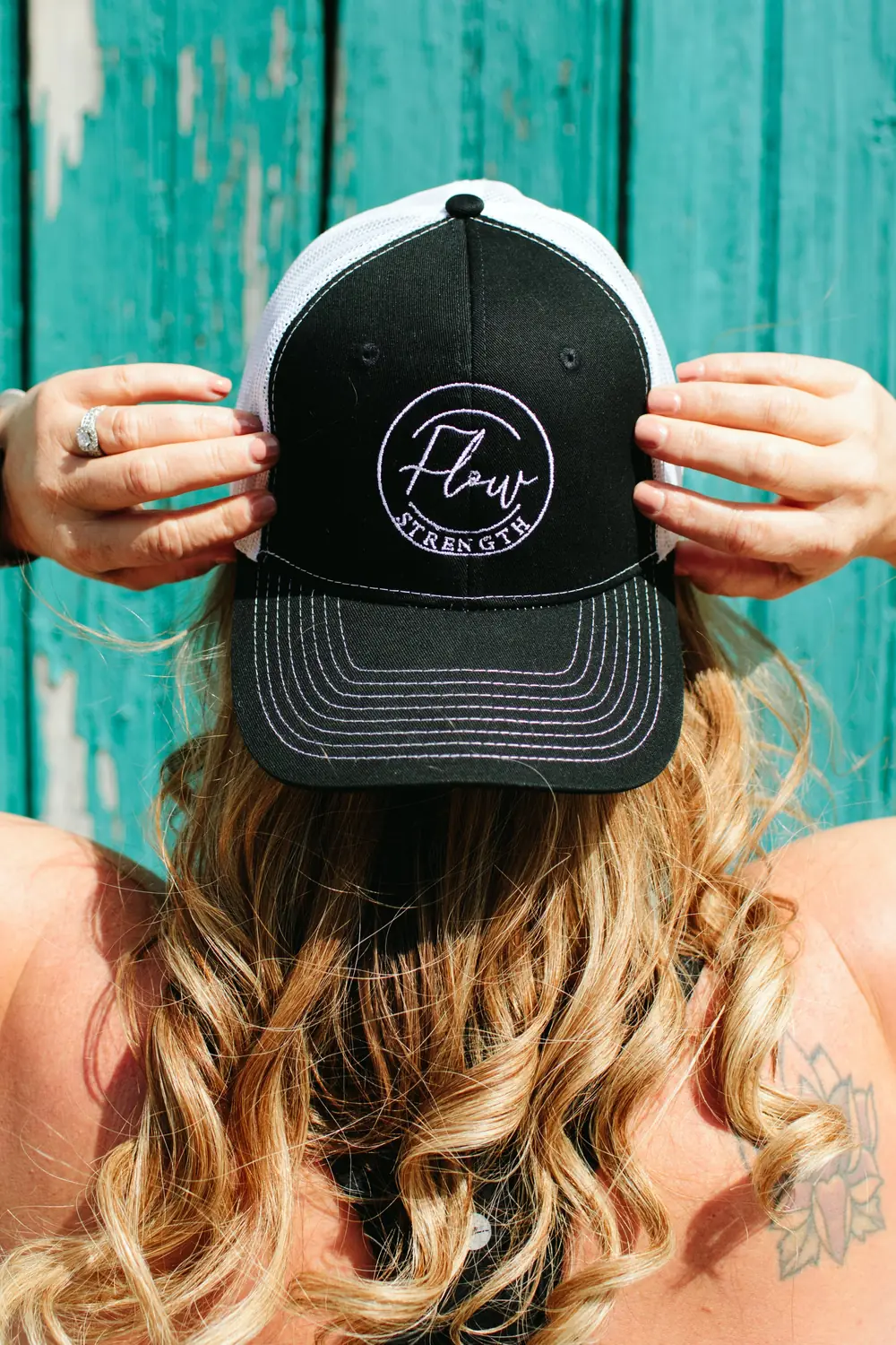 A Flow Strength trucker cap held against weathered teal barn board