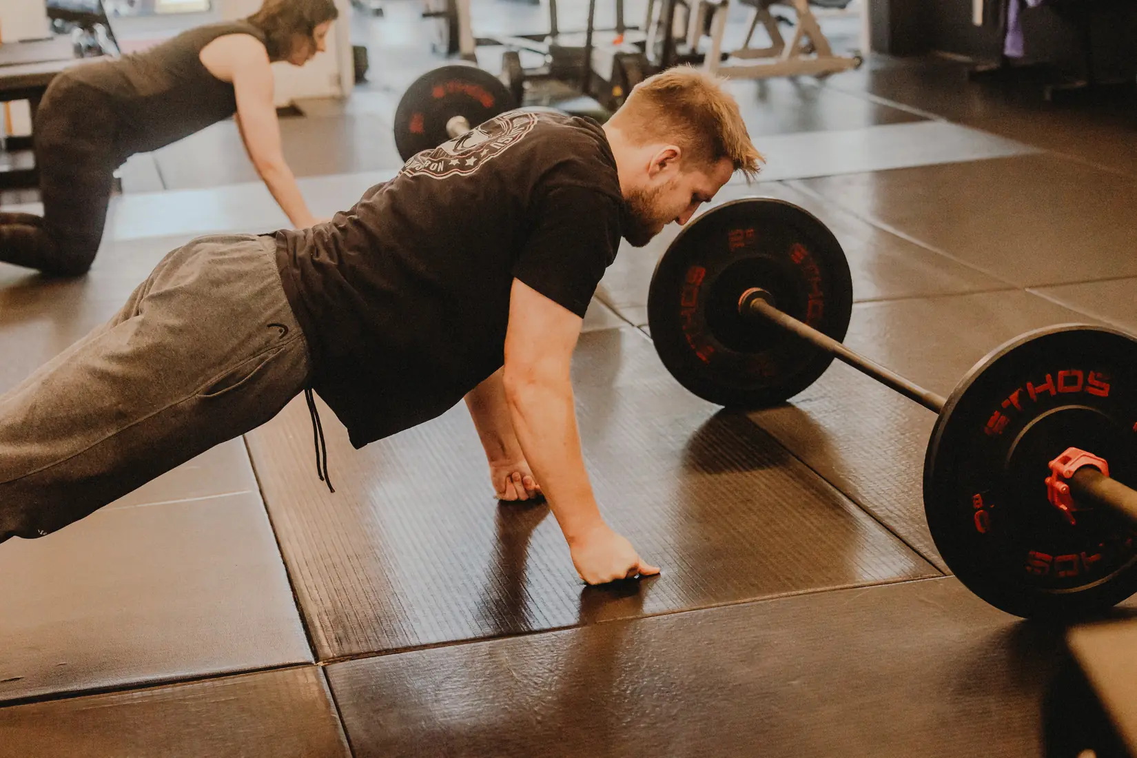 a member holding a plank beside a loaded barbell
